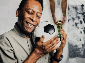 FOTO DE ARCHIVO: Un aficionado de Brasil sostiene una réplica del trofeo de la Copa del Mundo frente a una pancarta del exjugador brasileño Pelé antes del partido Camerún-Brasil