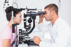 Male optician examining womans eyes through slit lamp in clinic